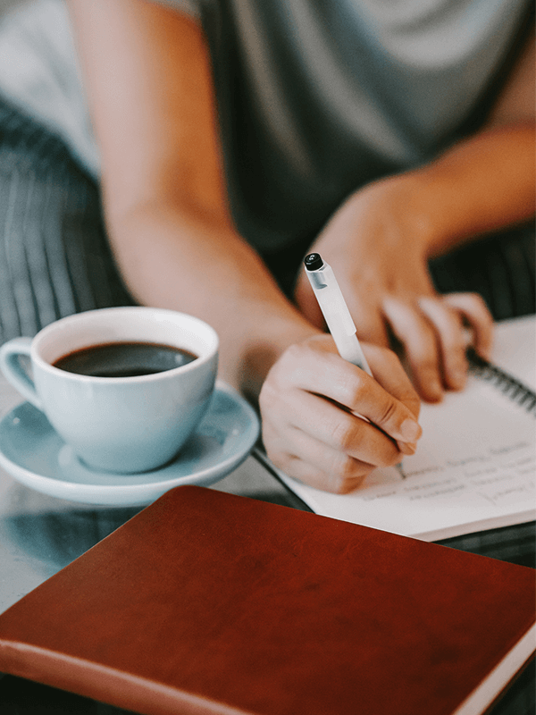 woman writing on a journal with a cup of coffee